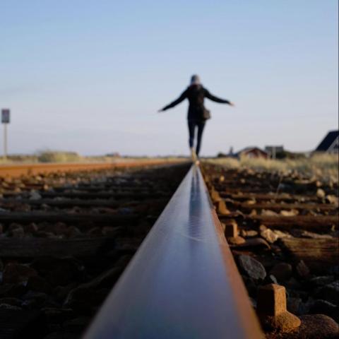 A person walks far down a train track rail with arms out for balance; low-angle shot focusing on the rail.